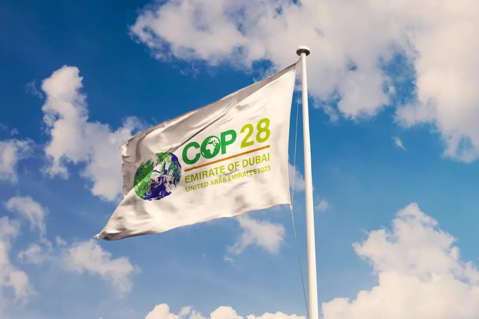 White flag with COP28 cliamte conference logo against lightly cloudy blue sky.